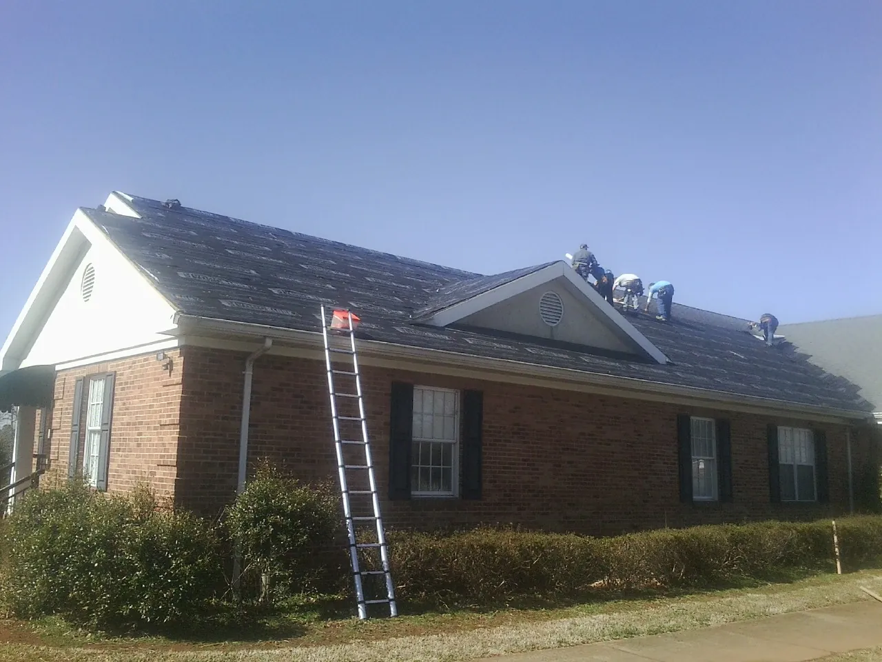 Crew tearing shingles off a brick ranch roof with a ladder set — Metal Roof Repair work by our crew in Bonne Terre