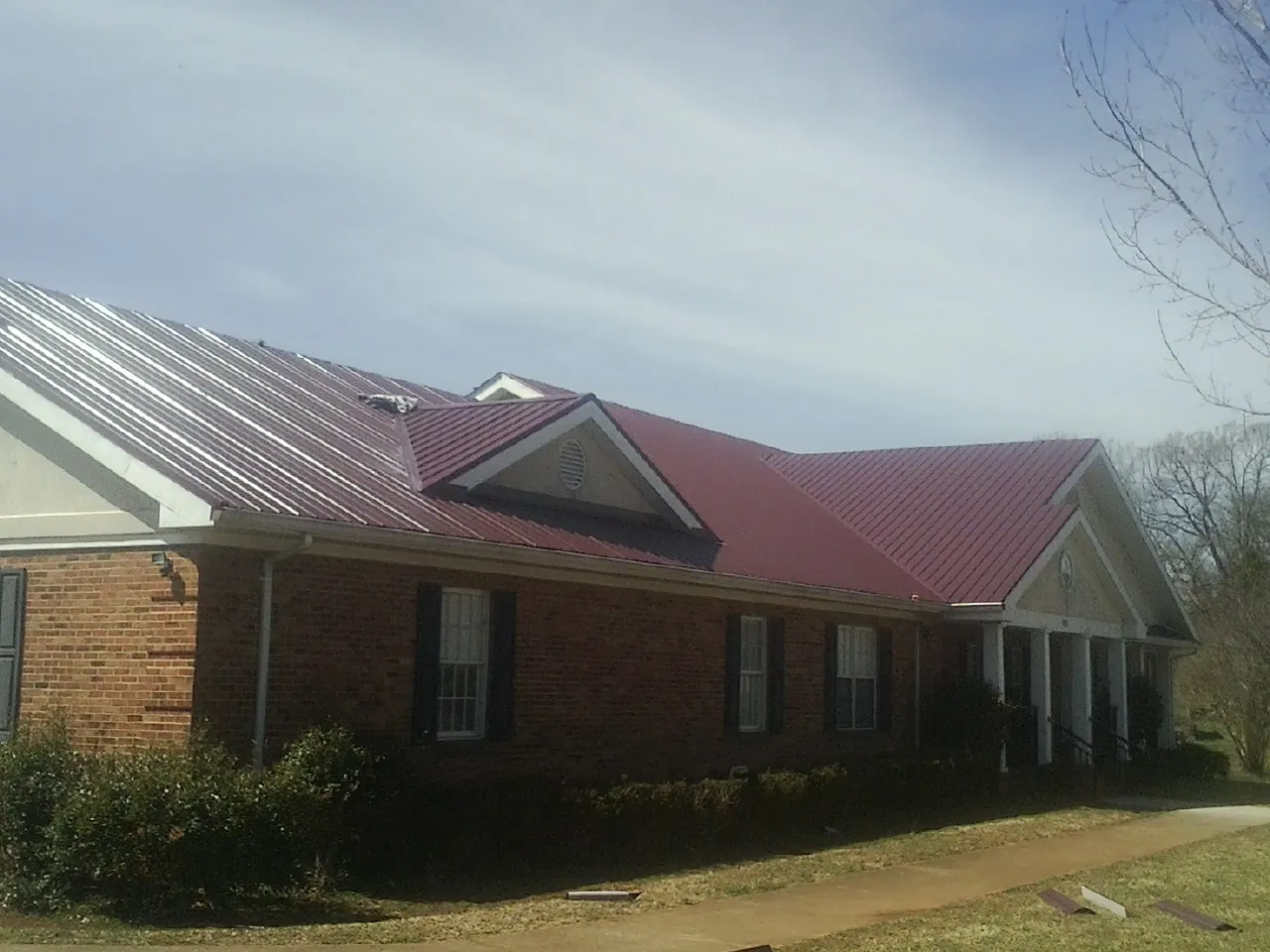 Red metal roof with gabled entries on a long brick building, from a Hail Damage Roof Repair job in Bonne Terre