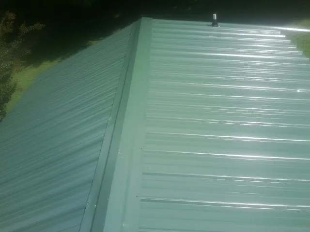 New green metal panels meeting at the ridge of a roof — Flat Roof Repair work by our crew in Bonne Terre