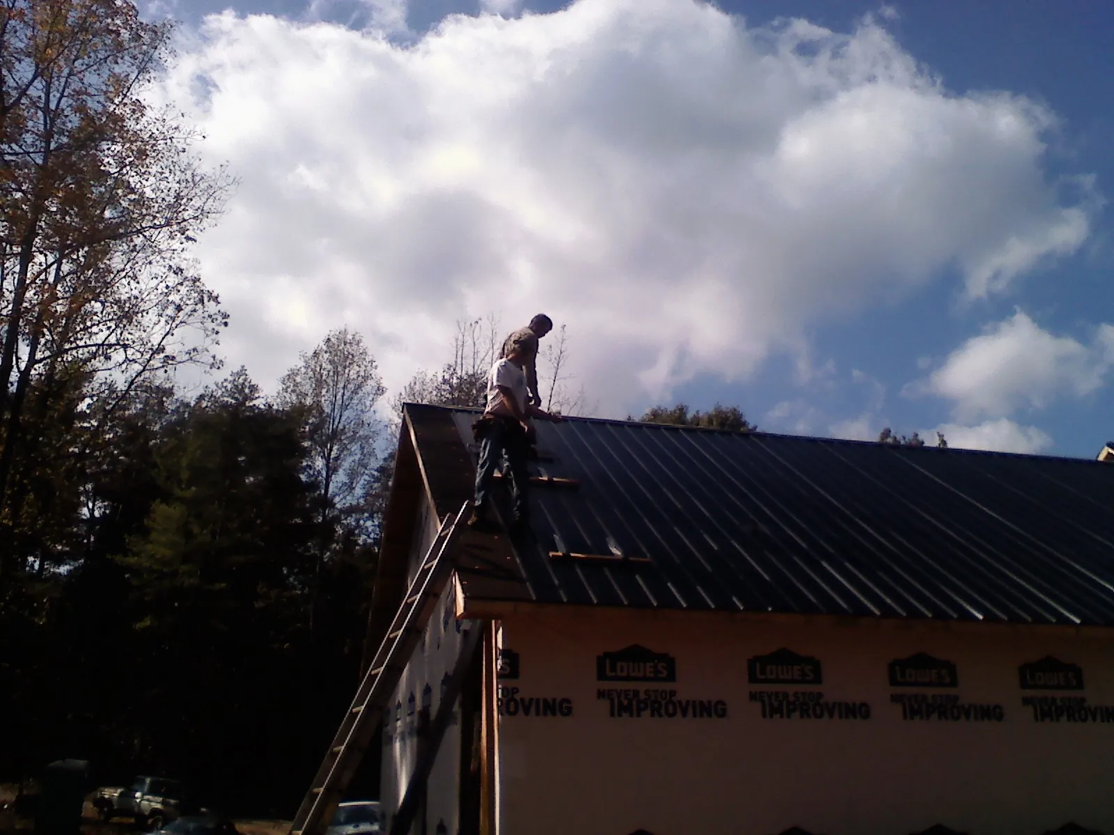 Roofer fastening dark metal panels high against a cloudy sky, from a Roof Inspection job in Bonne Terre