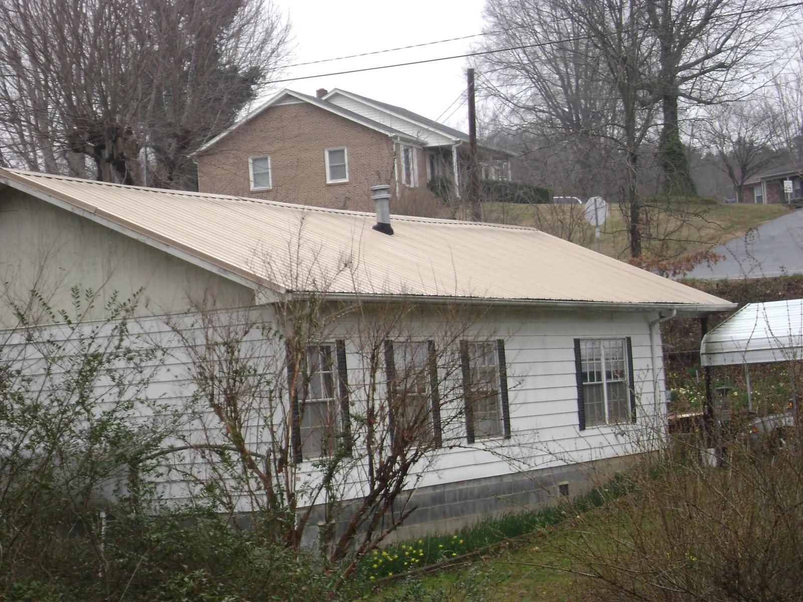 Tan metal roof on a white sided house set into a hillside — Commercial Roofing by Roofing Brothers in Bonne Terre
