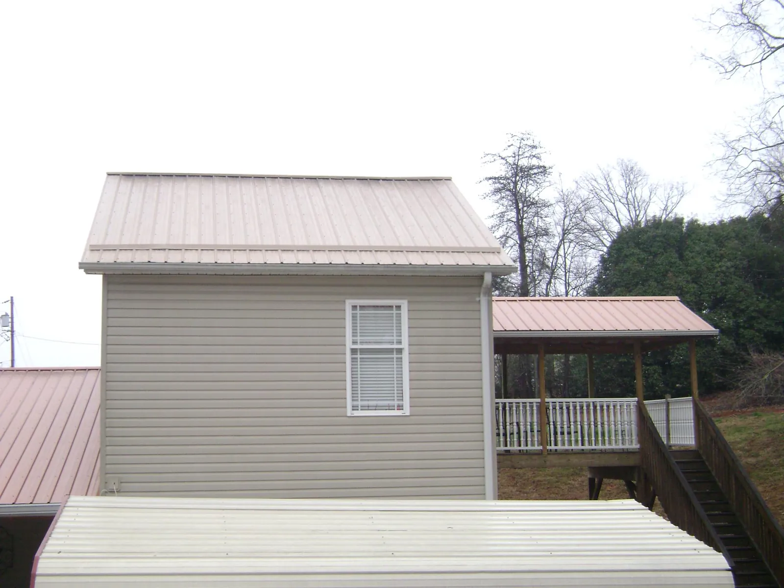 Tan metal roofs on a two story addition and attached porch, from a Roof Replacement job in Bonne Terre