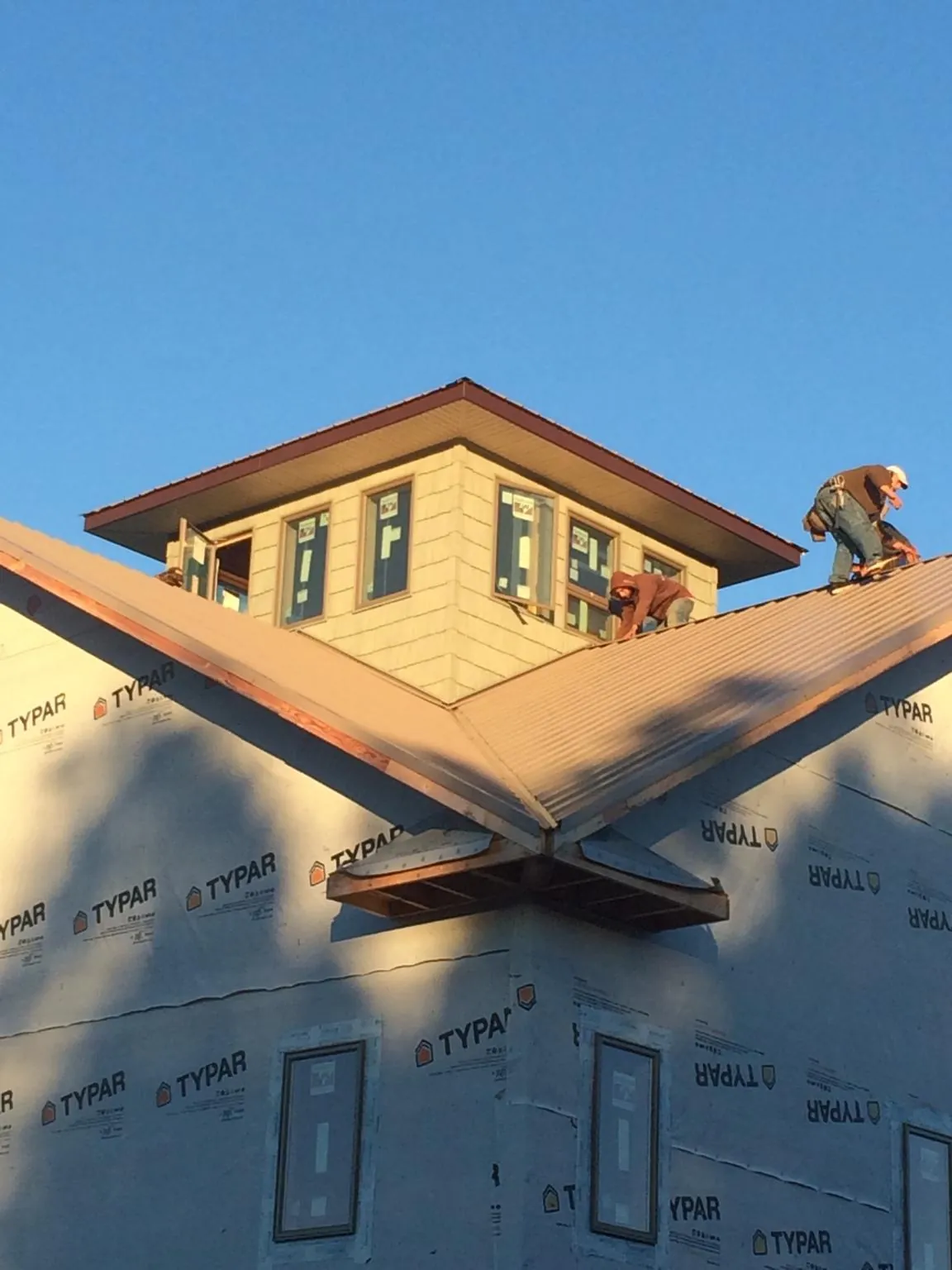 Roofers working around a rooftop cupola on a new metal roof at sunset — Roof Waterproofing in Bonne Terre by Roofing Brothers
